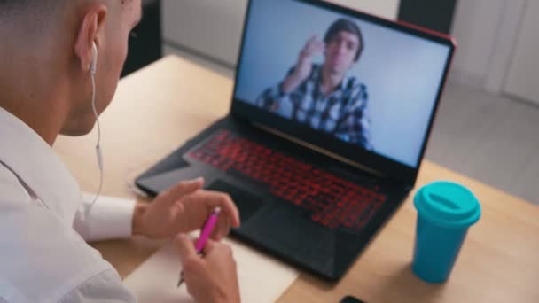 Hombre joven con auriculares viendo webinar en línea utilizando la llamada de conferencia web portátil en casa . — Vídeos de Stock