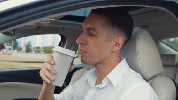 Porträt eines jungen Geschäftsmannes im weißen Hemd trinkt leckeren Kaffee sitzend im Auto am Fahrersitz. — Stockvideo