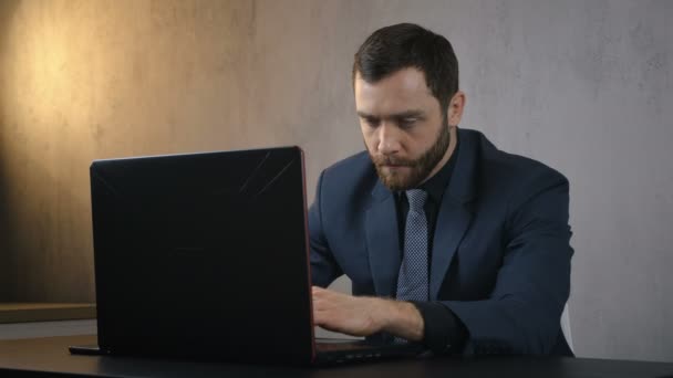 В офисе Бизнесмен сидит за столом, используя ноутбук, работая над проектом в ночное время — стоковое видео