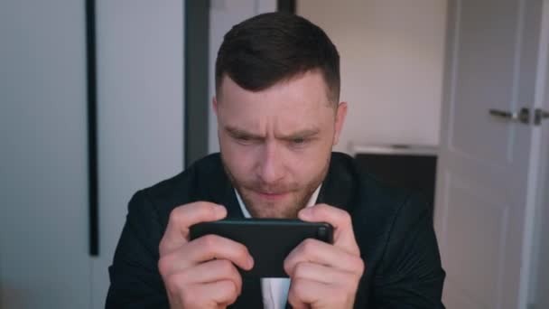 Junger Geschäftsmann spielt Online-Spiel auf Smartphone, während er im Home Office am Schreibtisch sitzt — Stockvideo