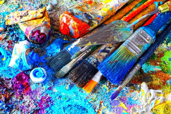 Фарби та пензлі, що лежать на пофарбованому фоні — стокове фото