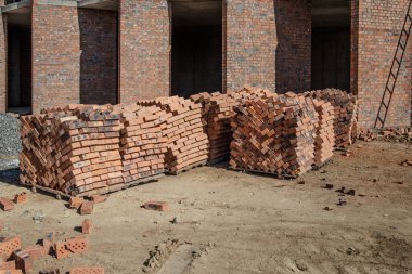 Yapının yanında duran turuncu kil tuğla paketleri var.