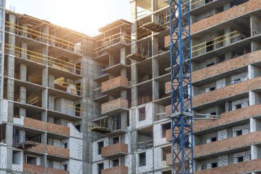 Yeni bir apartman bloğunda çalışma platformları sağlayan geniş kapsamlı yapı iskeleleri, inşaat halindeki uzun binalar, bir inşaat sahasındaki serbest kule vinci.