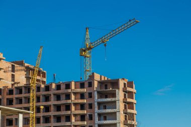 Yeni bir apartman bloğunda çalışma platformları sağlayan geniş kapsamlı yapı iskeleleri, inşaat halindeki uzun binalar, bir inşaat sahasındaki serbest kule vinci.