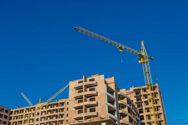 Yeni bir apartman bloğunda çalışma platformları sağlayan geniş kapsamlı yapı iskeleleri, inşaat halindeki uzun binalar, bir inşaat sahasındaki serbest kule vinci.