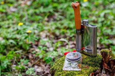 Ormandaki bir kütükte, orman çiçekleriyle birlikte bir fincan çay. Seyahat konsepti. Turist çeliği kupası ve yaz ormanlarında pusula. Doğanın arka planında bıçak.,