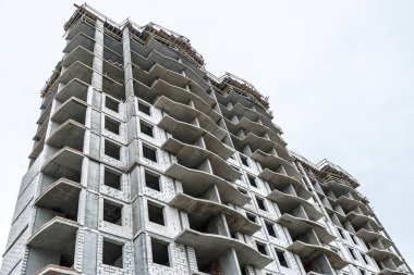 Yeni bir apartman bloğunda çalışma platformları sağlayan geniş kapsamlı yapı iskeleleri, inşaat halindeki uzun binalar, bir inşaat sahasındaki serbest kule vinci.