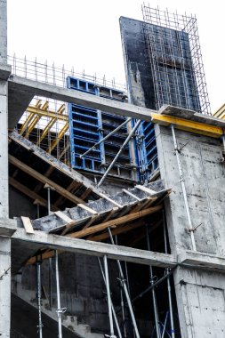 Yeni bir apartman bloğunda çalışma platformları sağlayan geniş kapsamlı yapı iskeleleri, inşaat halindeki uzun binalar, bir inşaat sahasındaki serbest kule vinci.