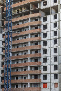 Yeni bir apartman bloğunda çalışma platformları sağlayan geniş kapsamlı yapı iskeleleri, inşaat halindeki uzun binalar, bir inşaat sahasındaki serbest kule vinci.