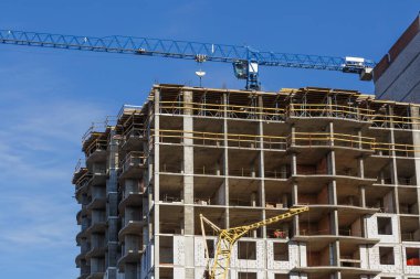 Yeni bir apartman bloğunda çalışma platformları sağlayan geniş kapsamlı yapı iskeleleri, inşaat halindeki uzun binalar, bir inşaat sahasındaki serbest kule vinci.