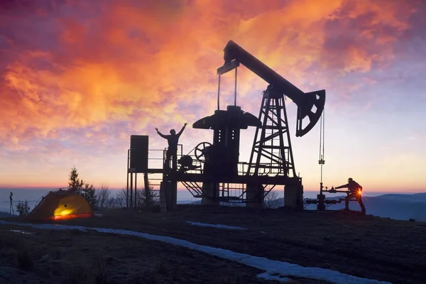 Ukrainian Carpathians with of oil and gas extraction and male silhouettes against sunset background