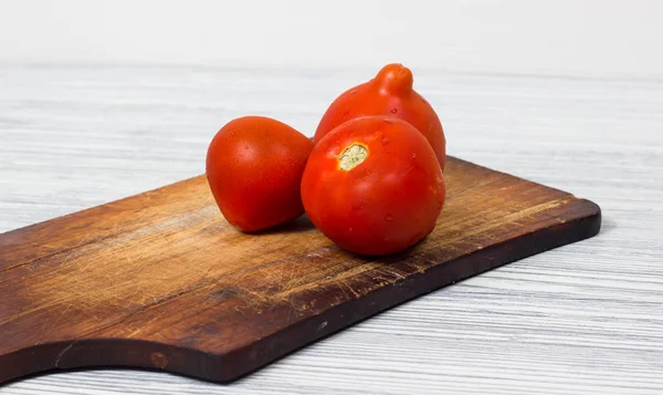 Fresh tomatoes on vintage wooden cutting board and wood background — Stock Photo, Image
