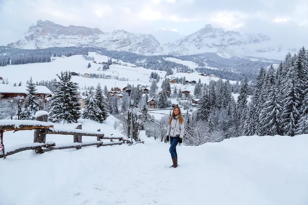 Hermosa chica de pie en las montañas durante el invierno con una vista asombrosa del pueblo de montaña —  Fotos de Stock