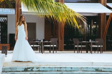 Güzel gelin gelinlik palmiye altında havuzun uzun beyaz bir elbise içinde poz