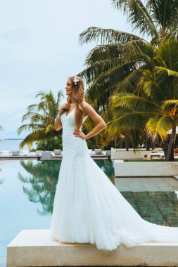 Mutlu gelin arasında güzel tropikal Peyzaj taş gazebo yanındaki ayakta. Deniz, gökyüzü, çiçekli bitkiler ve palmiye ağaçları içinde belgili tanımlık geçmiş. Düğün ve balayı konsepti. Retro fotoğraf.