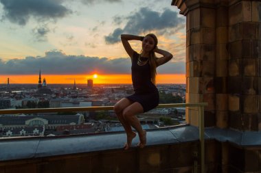 Riga, Letonya günbatımında Çatının kenarında oturan güzel kız