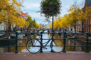 Şehir merkezinde gün batımında kanal. İnanılmaz bir Amsterdam görünümü ile köprü üzerinde bisiklet duran.