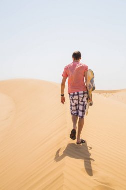 Dune bir sandboard ile tepesinde yürüyen adam.