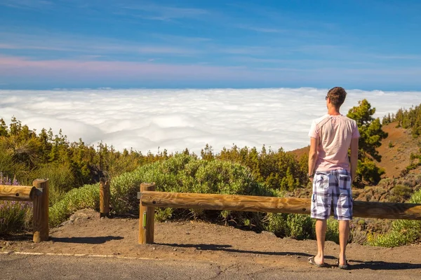 Young man standing on the edge of the world above the clouds looking into the horizon