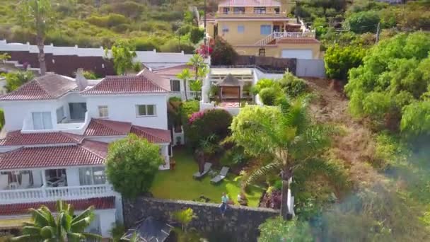 Jeune homme assis près de la villa sur l'île de Tenerife tandis que le drone s'envole loin de lui. Belle vue d'en haut sur l'île et la villa au bord de la falaise .