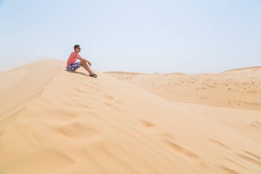 Bununla birlikte güneş gözlüklü bir çölde oturan genç çocuk