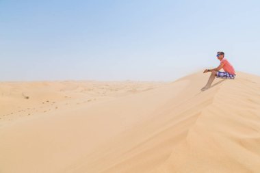 Bununla birlikte güneş gözlüklü bir çölde oturan genç çocuk