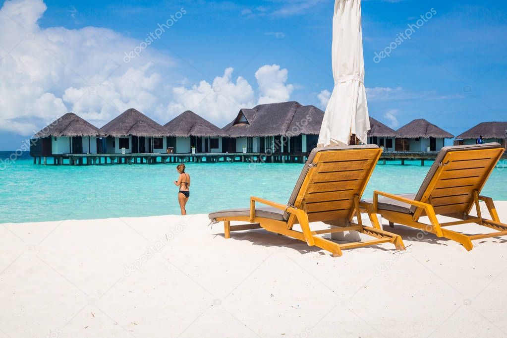Wooden chairs at white sand beach with water villas background, Maldives