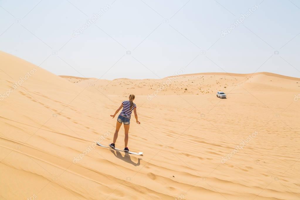 Woman sandboarding down the dune in a desert
