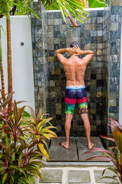 Tropik bir adada yağmur altında bir duş sahip genç adam