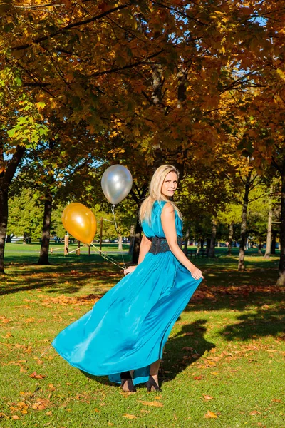 Beautiful young sexy lady in a dress standing in the park during golden autumn season with balloons in her hands