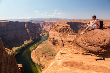 Uçurumun kenarında oturan genç adam. Büyük Kanyon, at ayakkabı dönemeçte şaşırtıcı görünümü.