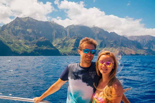 Beautiful couple sailing on a yacht down the Na Pali cliffs near Kauai island, Hawaii.