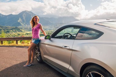 Güzel kız Ford Mustang Gt arkasında inanılmaz bir Hawaii manzaralı tarafından ayakta. Kayalıklarla, dağlar ve gün batımı. 30 Ağustos 2017. Hawaii, ABD.