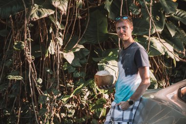 Genç adam orman holding ayakta bir taze hindistan cevizi içki elinde.