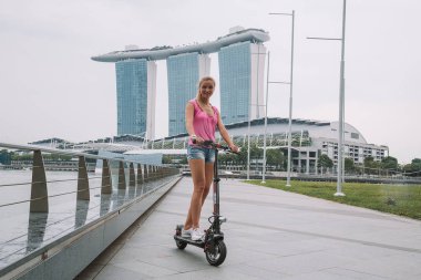 20 Mayıs 2017. Singapur. Şehrin üzerinde şaşırtıcı bir görünümü ile Singapur elektrikli bir scooter sürme genç sevimli kız.