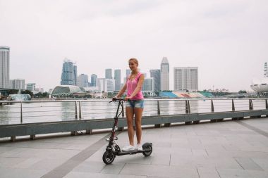 20 Mayıs 2017. Singapur. Şehrin üzerinde şaşırtıcı bir görünümü ile Singapur elektrikli bir scooter sürme genç sevimli kız.