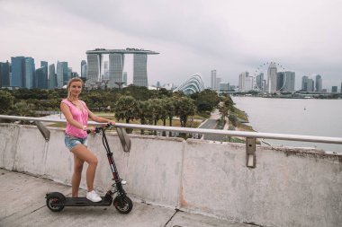 20 Mayıs 2017. Singapur. Şehrin üzerinde şaşırtıcı bir görünümü ile Singapur elektrikli bir scooter sürme genç sevimli kız.
