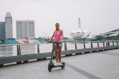 20 Mayıs 2017. Singapur. Şehrin üzerinde şaşırtıcı bir görünümü ile Singapur elektrikli bir scooter sürme genç sevimli kız.