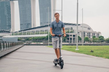 Genç adam şehre şaşırtıcı bir görünümü ile Singapur elektrikli bir scooter sürme.