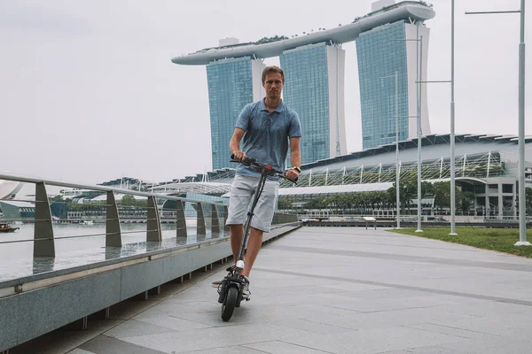 Genç adam şehre şaşırtıcı bir görünümü ile Singapur elektrikli bir scooter sürme.