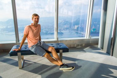 30 Ağustos 2017. Hong Kong. Çin. Genç adam Hong Kong gökdelen penceresinde kenarında otururken yukarıdan şehir izlerken.