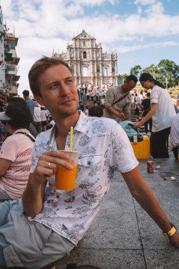 Makao, Çin - 30 Ağustos 2017: Ruins St.Paul Kilisesi tarafından oturan, Pastel De Nata yeme ve papaya suyu içme genç adam.
