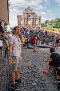 Makao, Çin - 30 Ağustos 2017: Ruins St.Paul Kilisesi tarafından oturan, Pastel De Nata yeme ve papaya suyu içme genç adam.