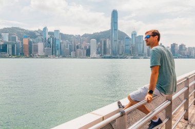 Hong Kong, Çin. 30 Ağustos 2017. Suyu içme Victoria Harbor şehir manzarası panorama üzerinden izlerken Hong Kong sahil şeridi üzerinde oturan genç adam.