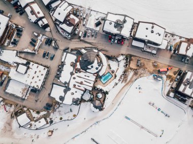 Aerial view of the ski resort winter town or village in the Alps with small houses, outdoor pool ski lifts and slopes clipart
