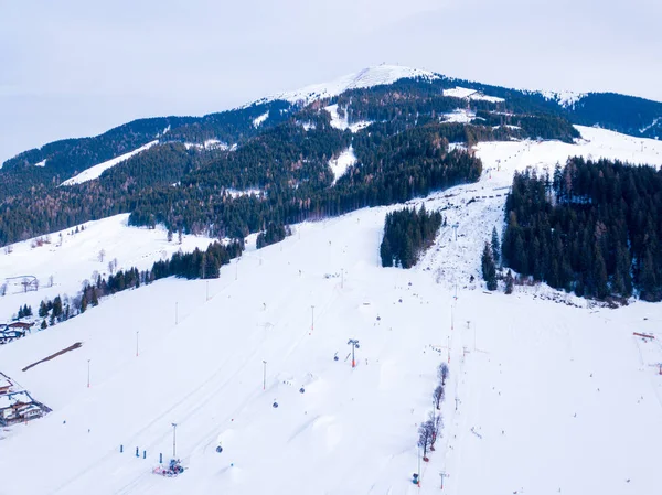 Aerial view of the mountain ski resort village in Austrian Alps with large mountain slopes, skiers, snowboarders, ski lifts and small winter town.