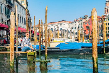Venedik, İtalya. 10 Nisan 2018. Venedik keşfetmek bir genç adam. Rialto Köprüsü yanı sıra San Marco Meydanı geçirerek gondol izlerken Kanallar başına oturmuş. 
