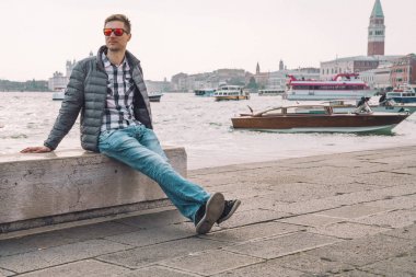 Venedik, İtalya. 10 Nisan 2018. Venedik keşfetmek bir genç adam. Rialto Köprüsü yanı sıra San Marco Meydanı geçirerek gondol izlerken Kanallar başına oturmuş.