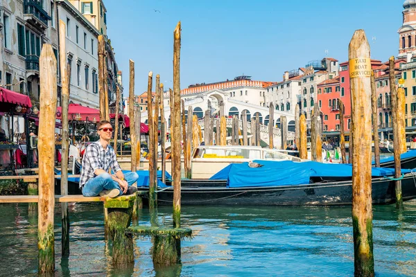 Venedik, İtalya. 10 Nisan 2018. Venedik keşfetmek bir genç adam. Rialto Köprüsü yanı sıra San Marco Meydanı geçirerek gondol izlerken Kanallar başına oturmuş. 
