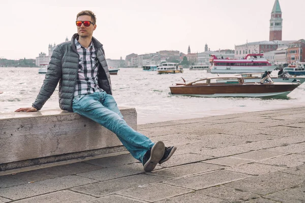 Venedik, İtalya. 10 Nisan 2018. Venedik keşfetmek bir genç adam. Rialto Köprüsü yanı sıra San Marco Meydanı geçirerek gondol izlerken Kanallar başına oturmuş.